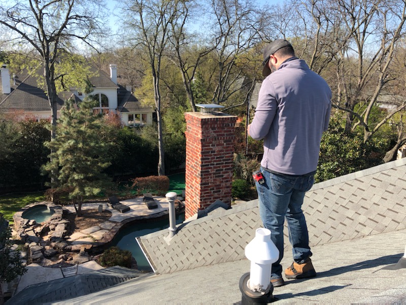 Inspector examining shingle roof near chimney